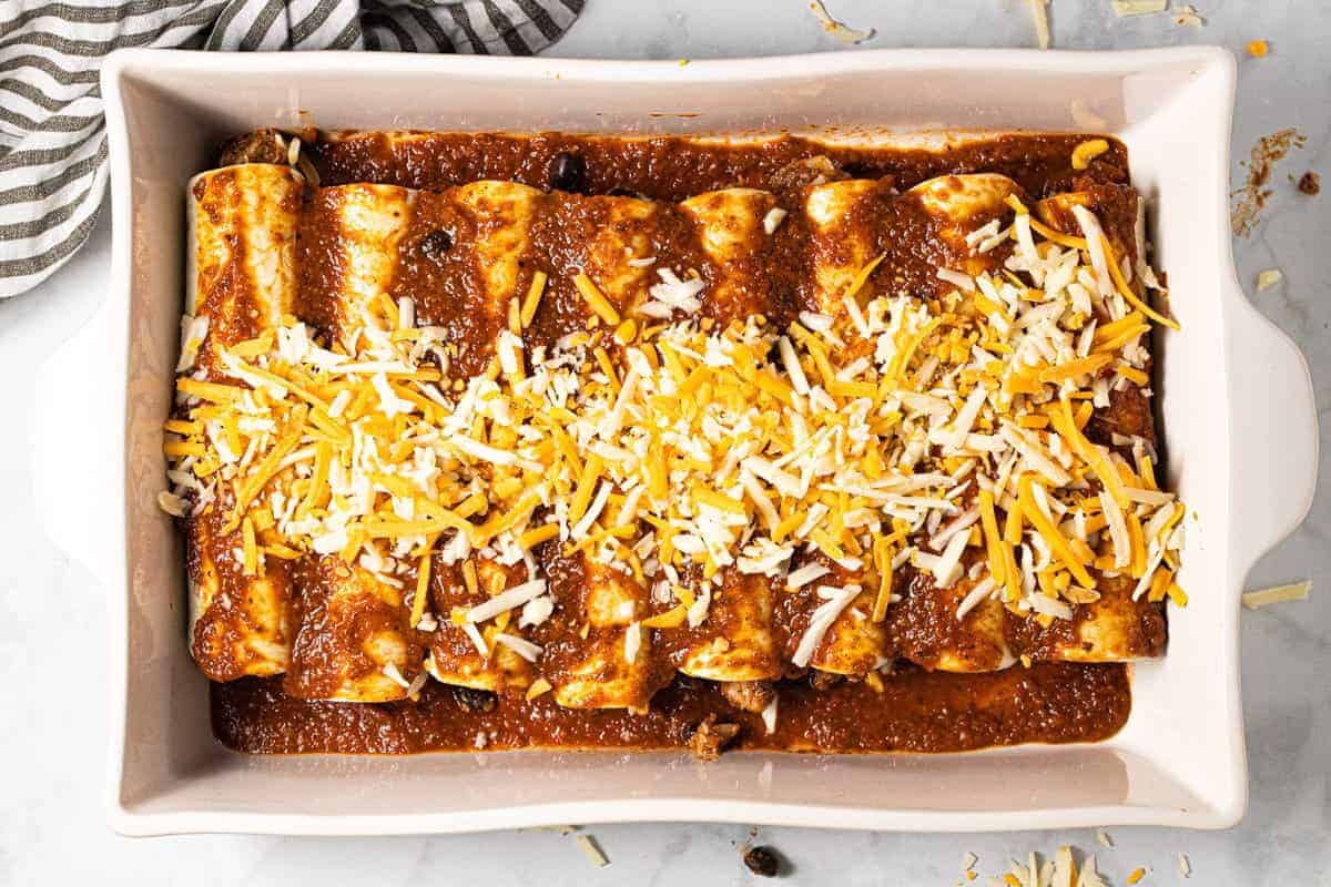 A baking dish filled with cheesy chicken enchiladas assembled and ready to go in the oven