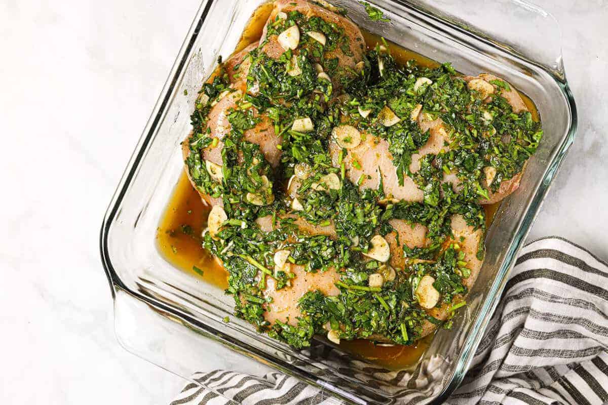 Square glass baking dish with raw chicken breast marinating in cilantro lime marinade