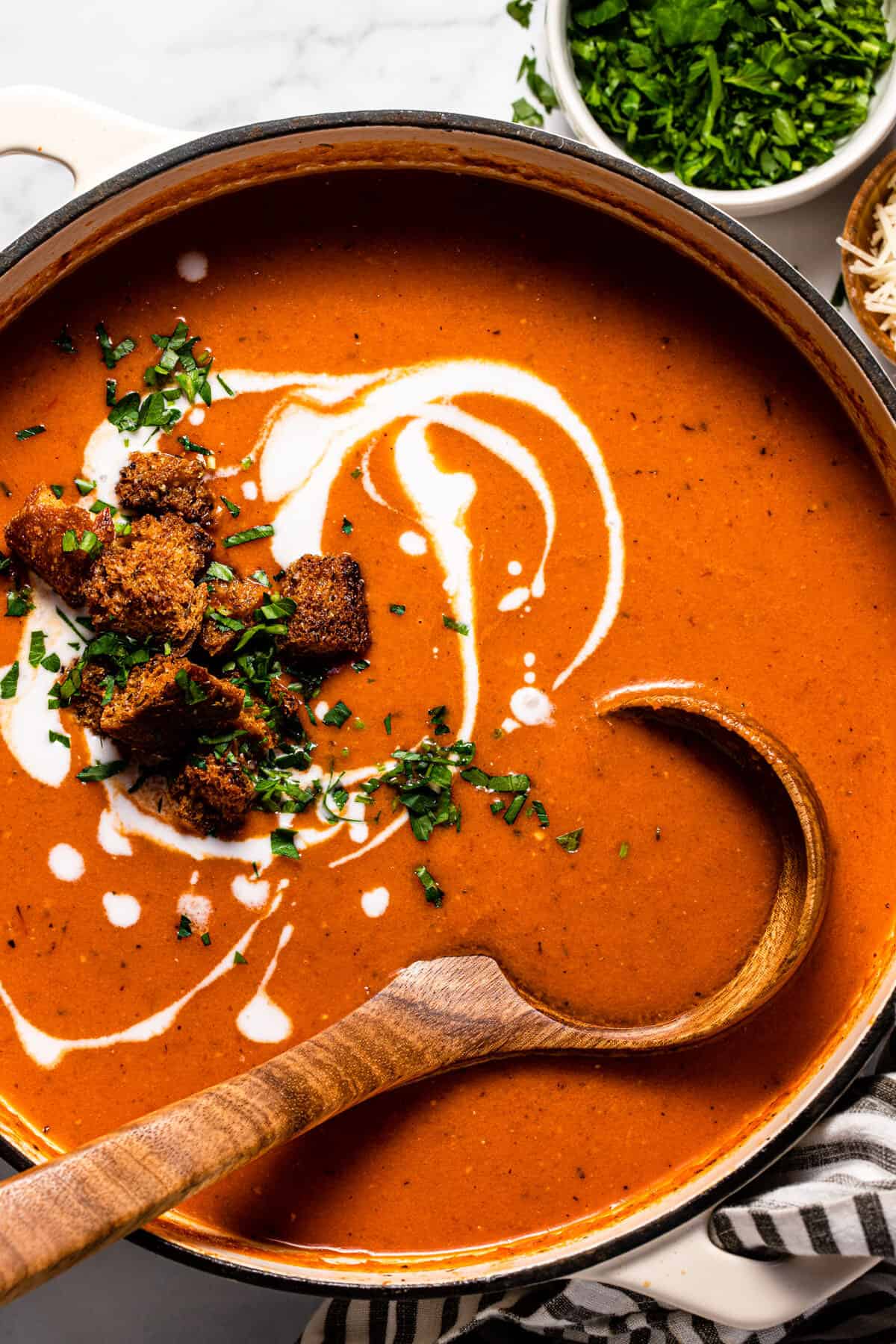 Large pot filled with creamy vegan tomato soup garnished with croutons