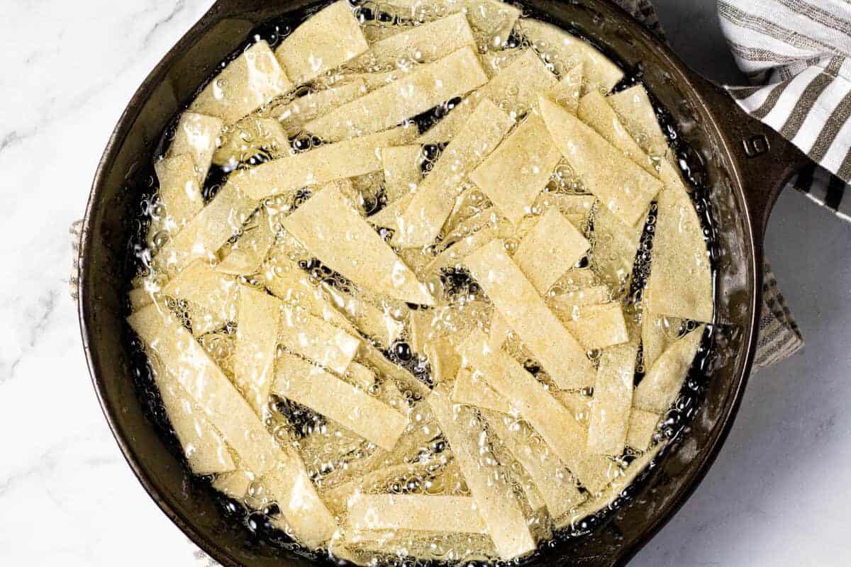 Cast iron pan with tortilla strips frying in oil 