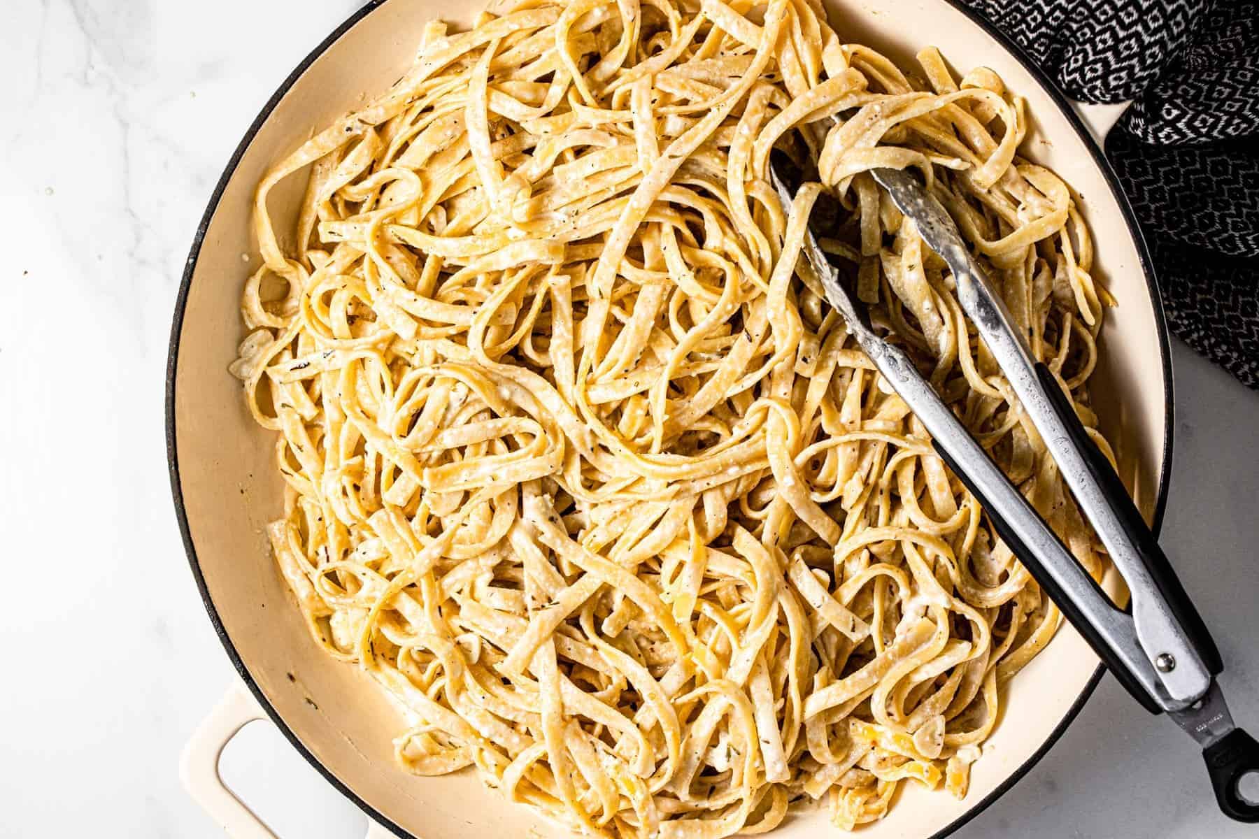 Large white pan filled with fettuccine pasta tossed in a creamy herb feta sauce