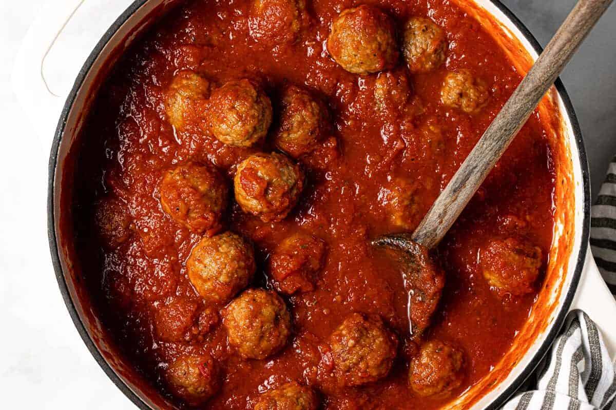 Large white pot filled with crushed tomatoes and meatballs