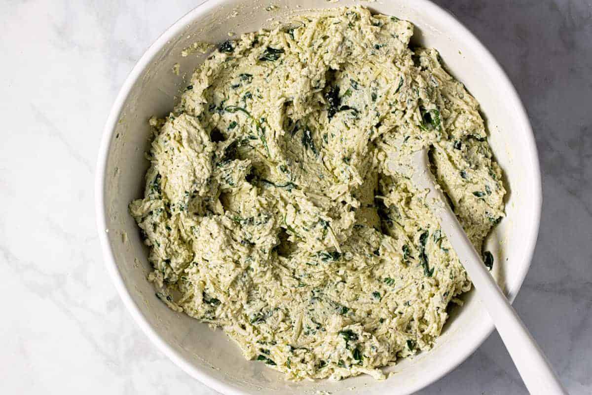 Large white bowl filled with ingredients to make manicotti filling