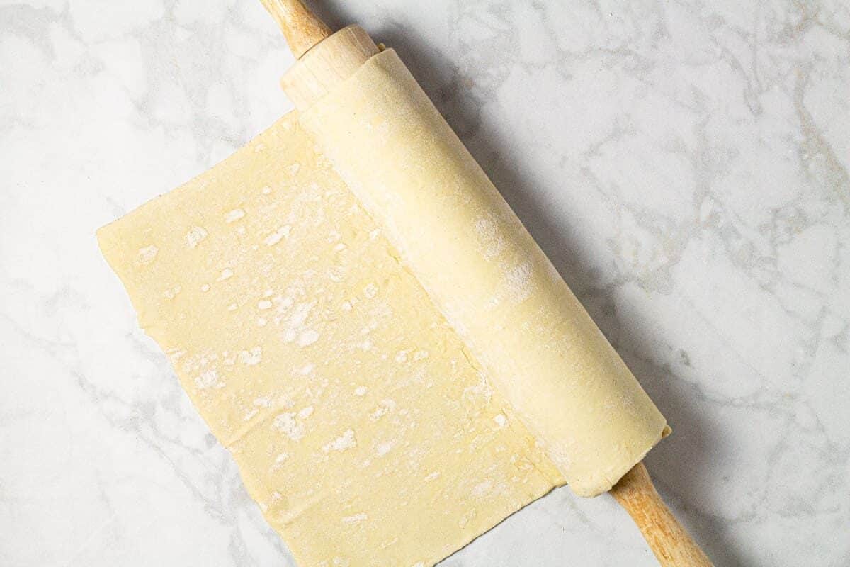 Gray marble counter top with puff pastry dough wrapped around a wooden rolling pin 