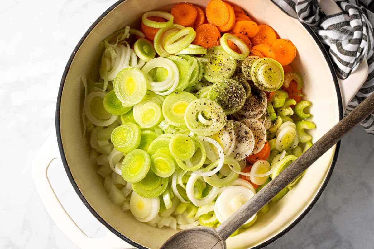 Large white pot filled with onion carrot celery and leeks