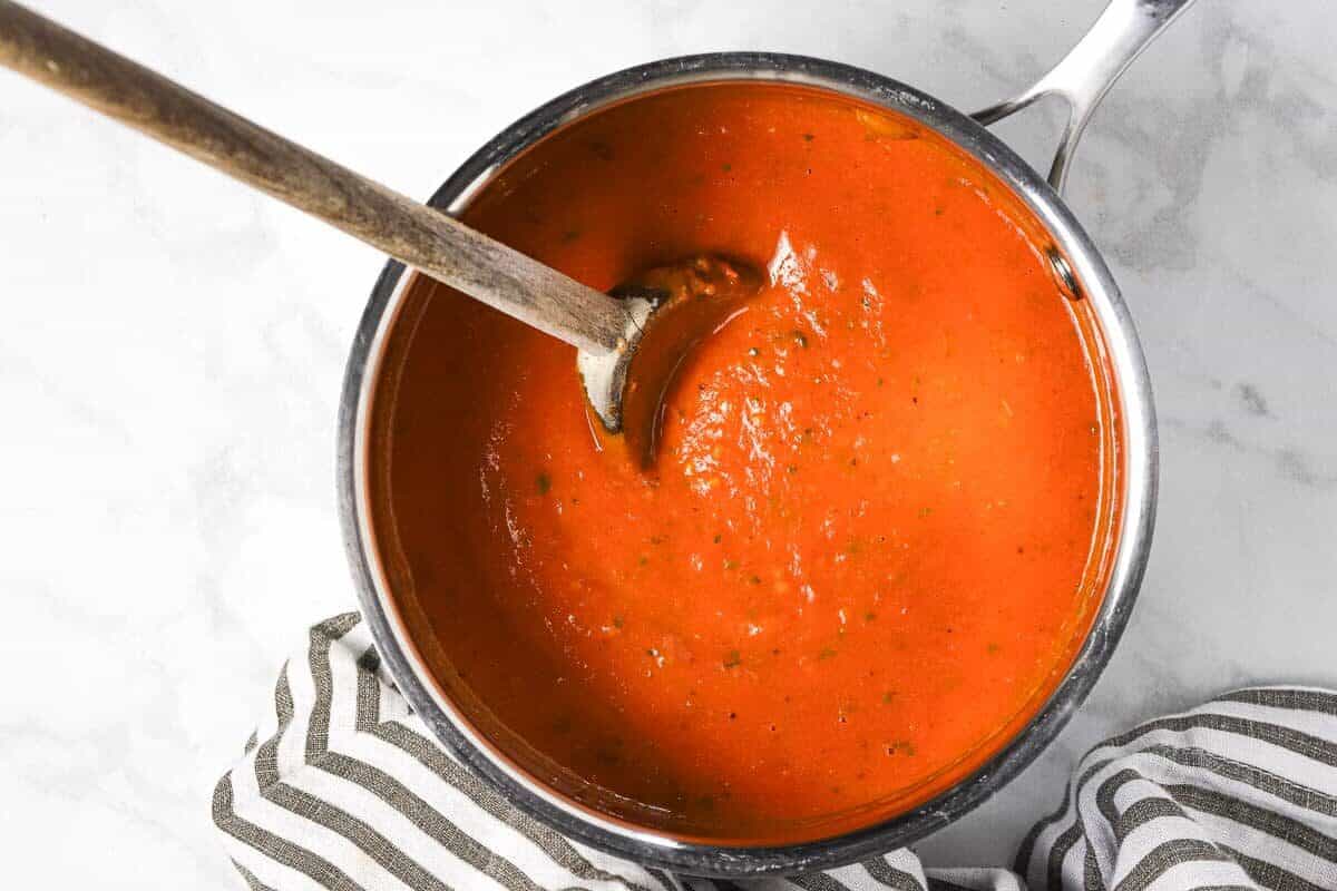 Small silver pot with creamy tomato sauce and a wooden spoon
