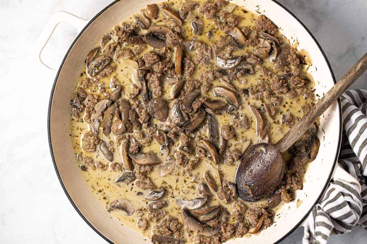 White pan filled with sausage sliced mushroom shredded Parmesan and heavy cream 