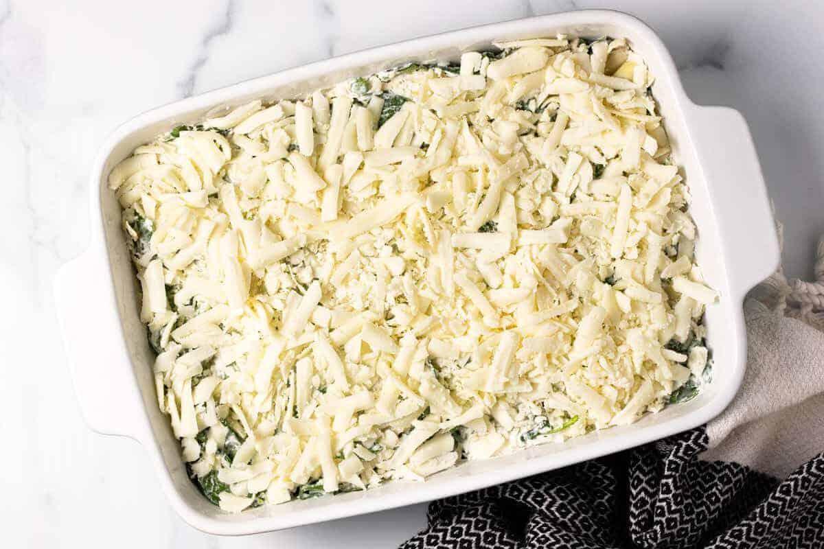 Spinach and artichoke dip spread in a large baking dish topped with shredded mozzarella