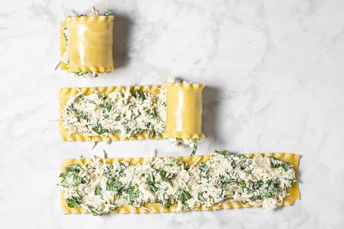 3 lasagna noodles with filling being rolled up on a white marble counter top