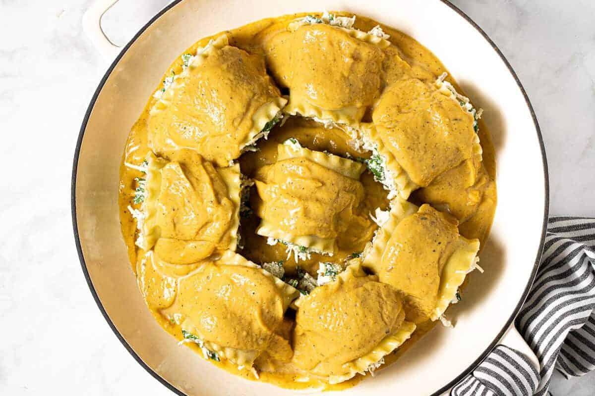 Squash lasagna roll ups in a white pan topped with creamy squash sauce