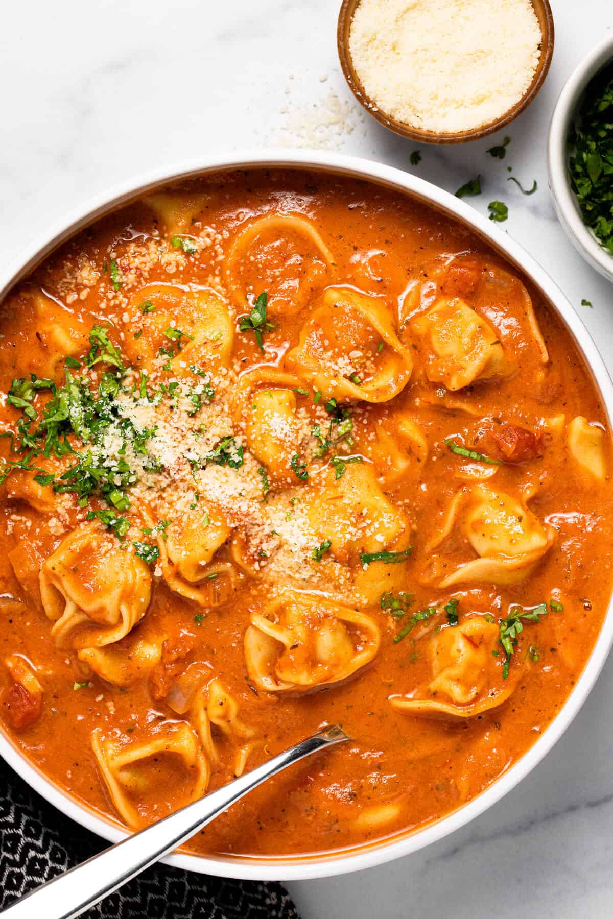 Overhead shot of a bowl of tomato tortellini soup garnished with Parmesan and parsley