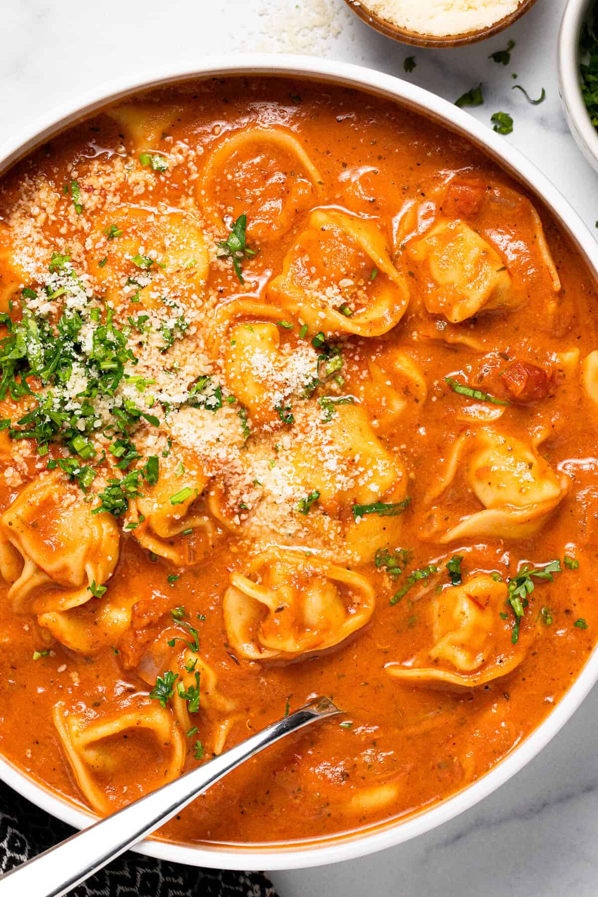 Overhead shot of a bowl of tomato tortellini soup garnished with Parmesan and parsley