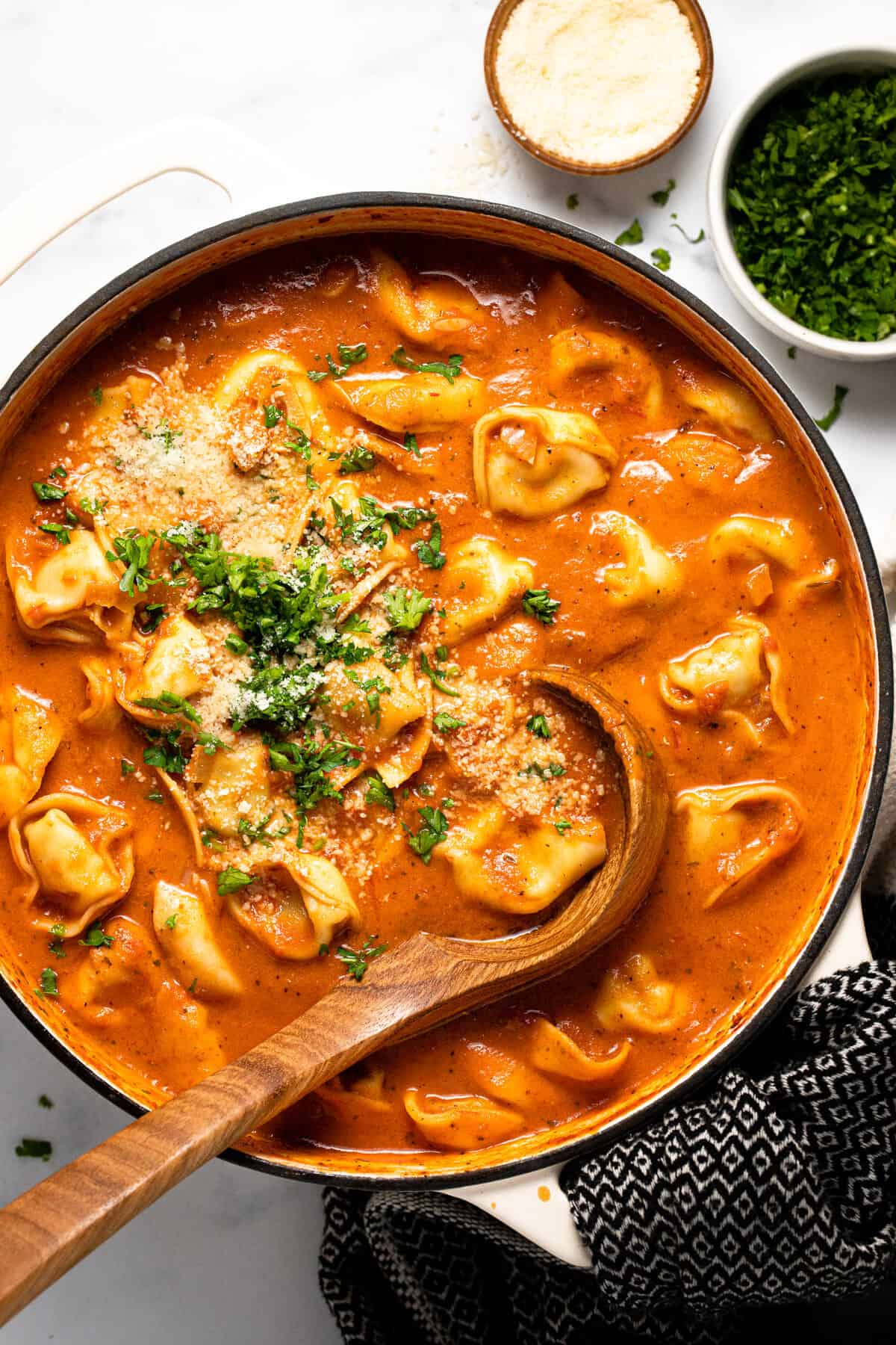 Large white pot filled with homemade tomato tortellini soup garnished with Parmesan