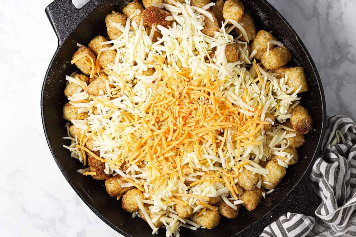 Tater tots in a cast iron skillet topped with shredded cheese