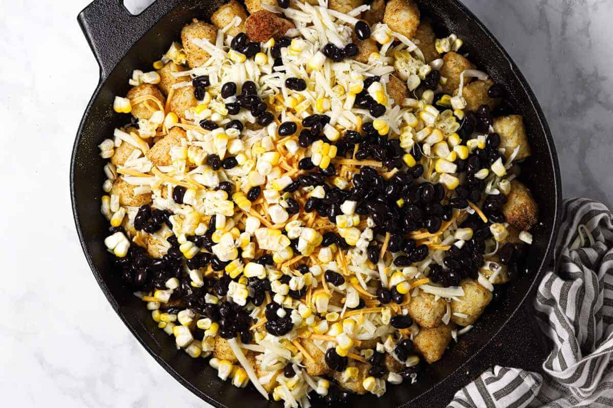 Tater tots in a cast iron skillet topped with cheese black beans and corn 