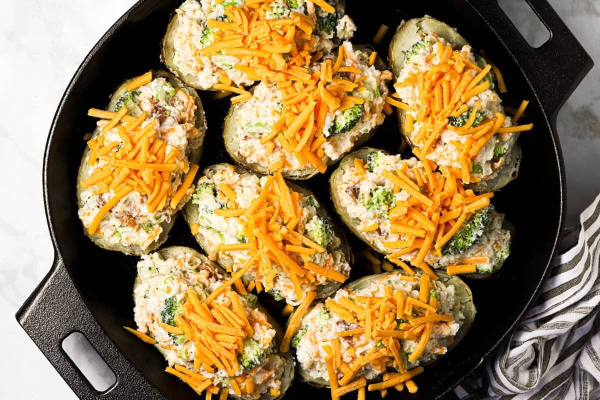 Large cast iron pan filled with assembled twice baked potatoes garnished with sour cream and sliced green onion