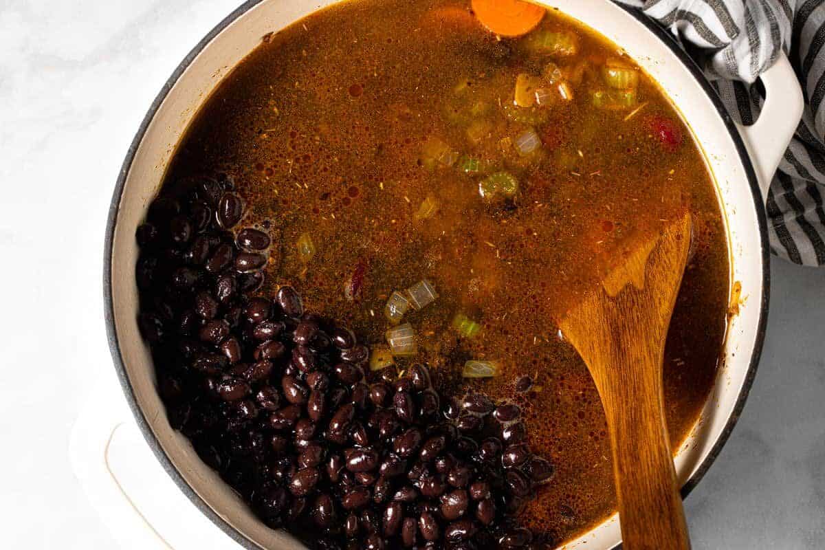 Large white pot filled with ingredients to make homemade creamy black bean soup 