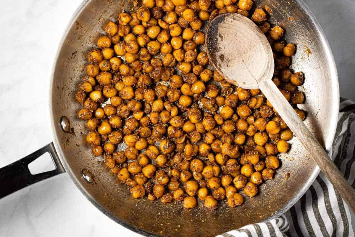 Metal pan filled with sauteed chickpeas and a wooden spoon