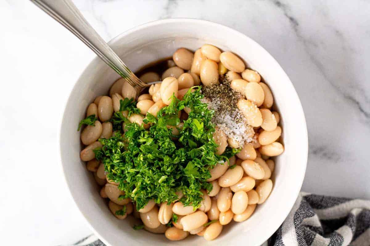 White bowl with Great Northern beans fresh parsley salt and pepper