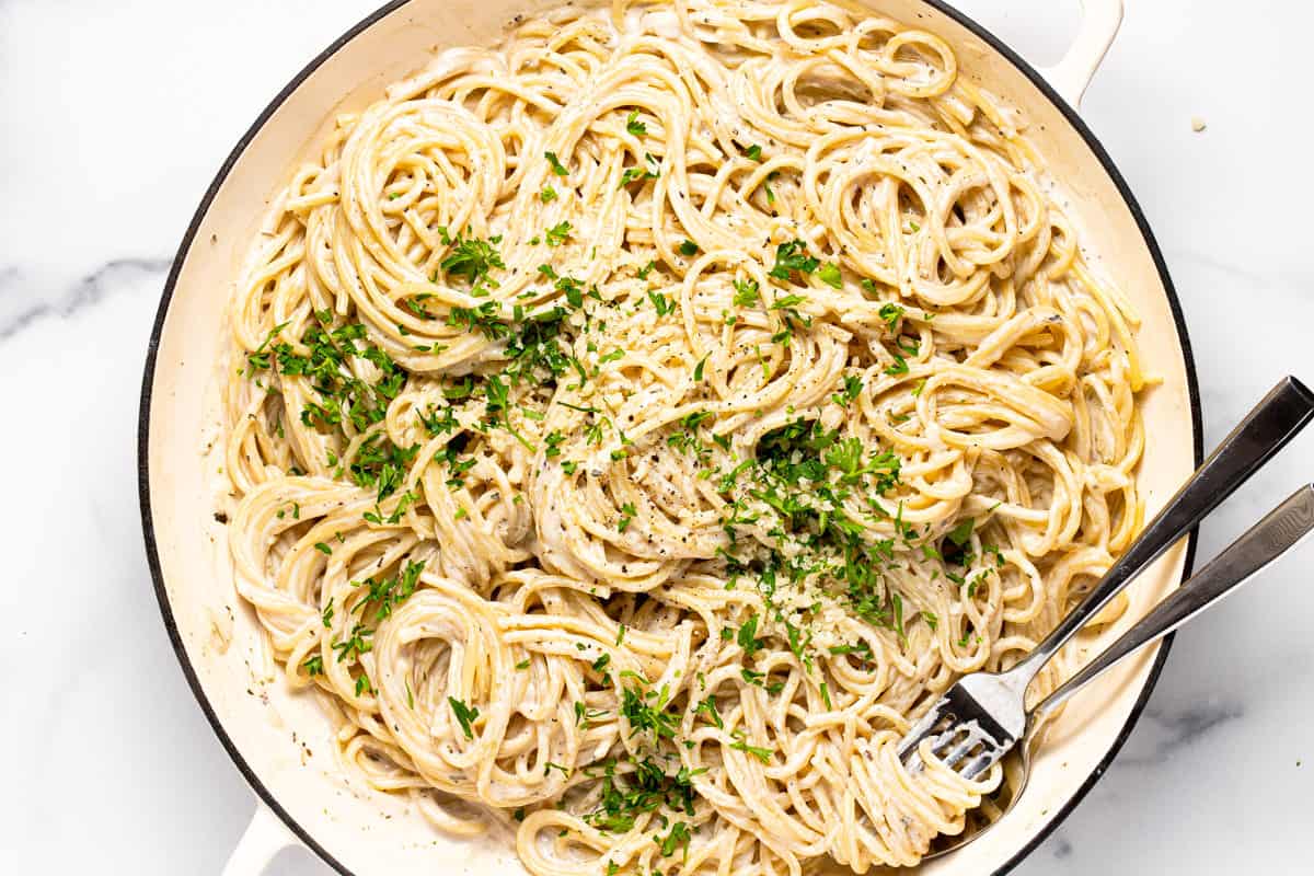 Large white pan filled with creamy garlic pasta garnished with fresh parsley 