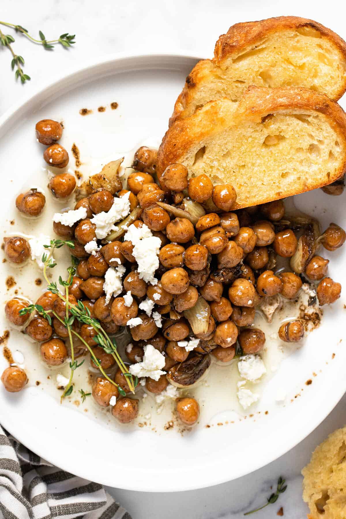 White plate filled with braised chickpeas and a couple slices of crusty bread