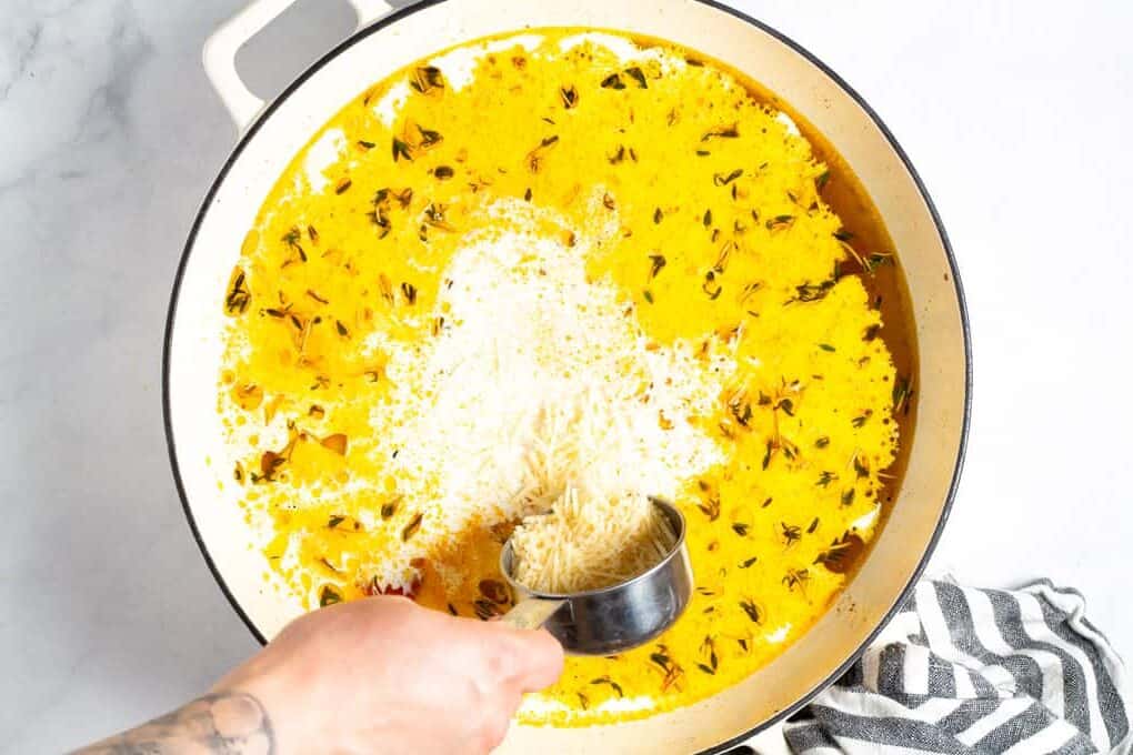 A large saute pan filled with veggies broth and cream with Parmesan cheese being added in 