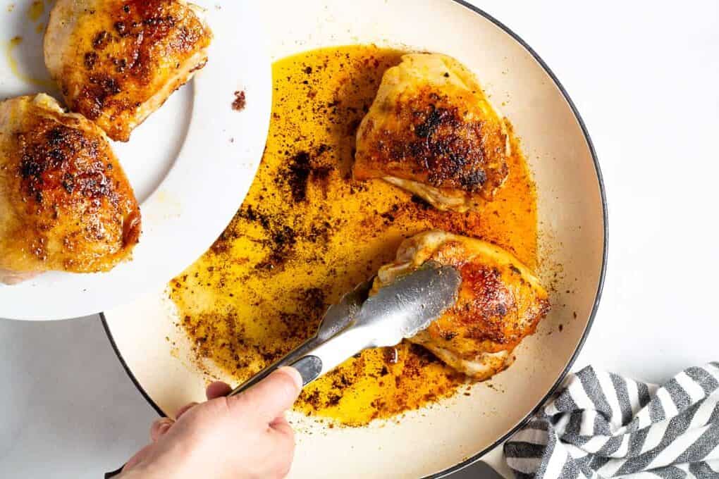 Tongs removing seared chicken thighs from a large pan 