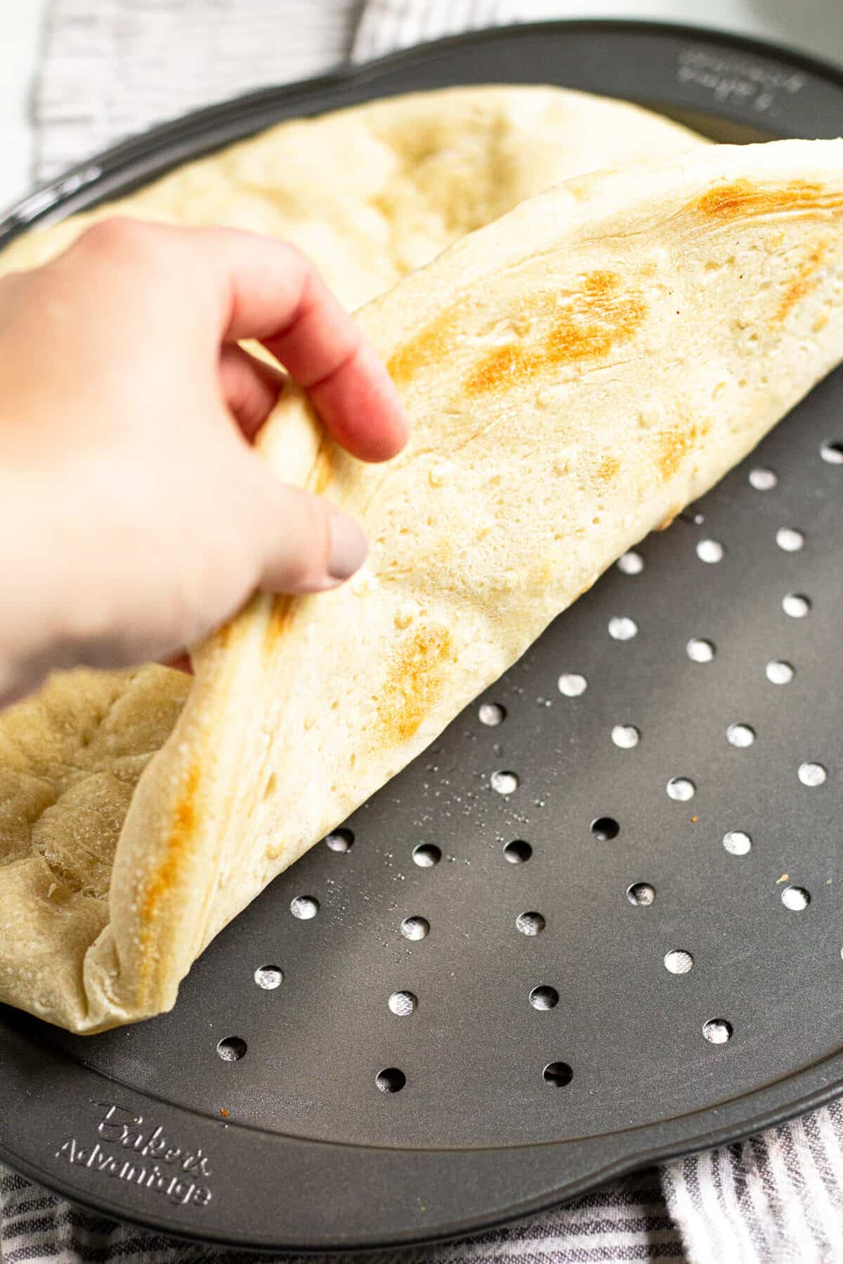 Pizza dough on a pizza pan that is partially baked and being folded to show you the under side 