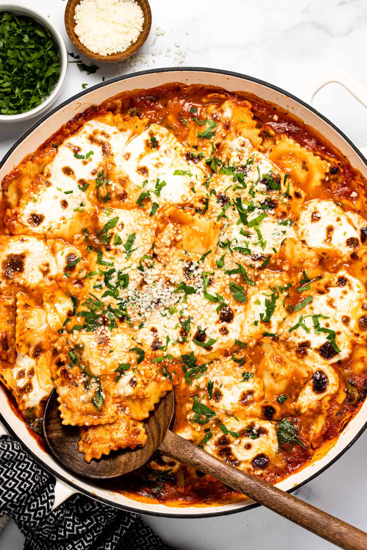 Large white pan filled with baked ravioli casserole garnished with fresh parsley