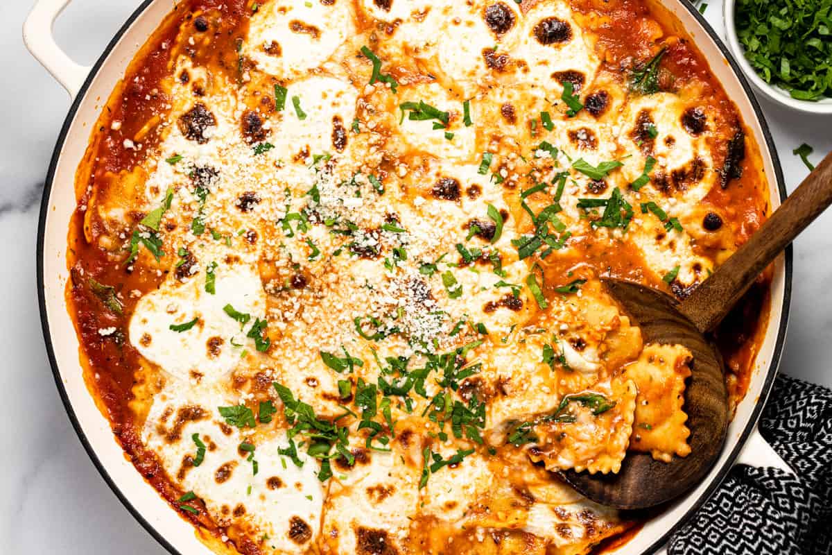 Large white pan filled with ingredients to make baked ravioli casserole