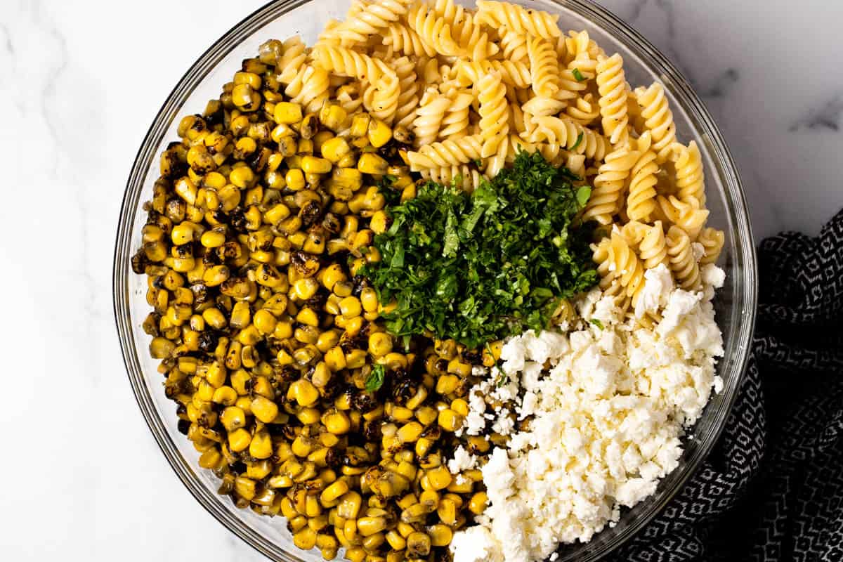 Large glass bowl filled with ingredients to make Mexican street corn pasta salad