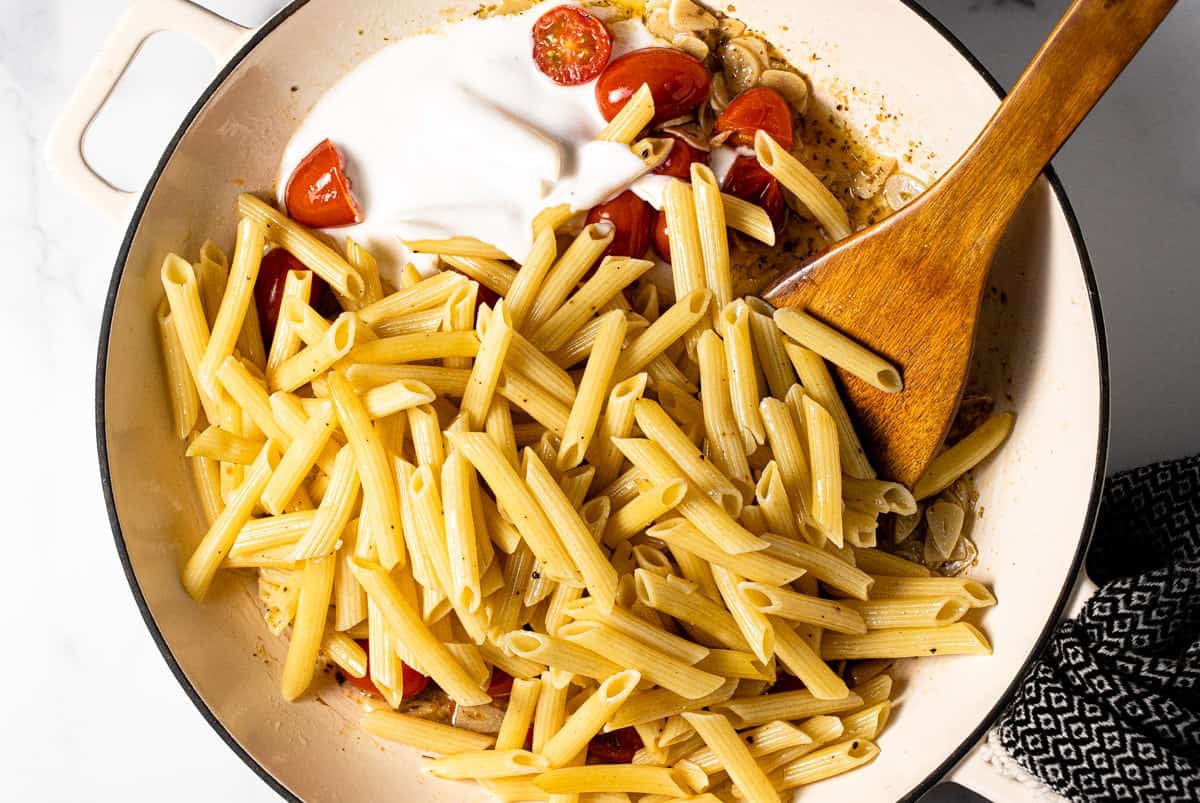 Large white pan filled with ingredients to make pasta with tomatoes and garlic cream sauce
