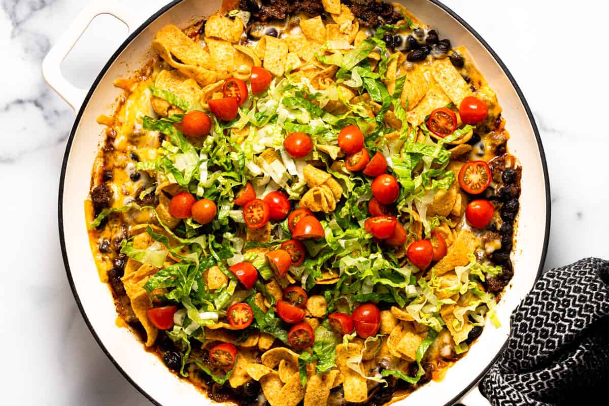 Large white pan filled with walking taco casserole topped with lettuce and tomato