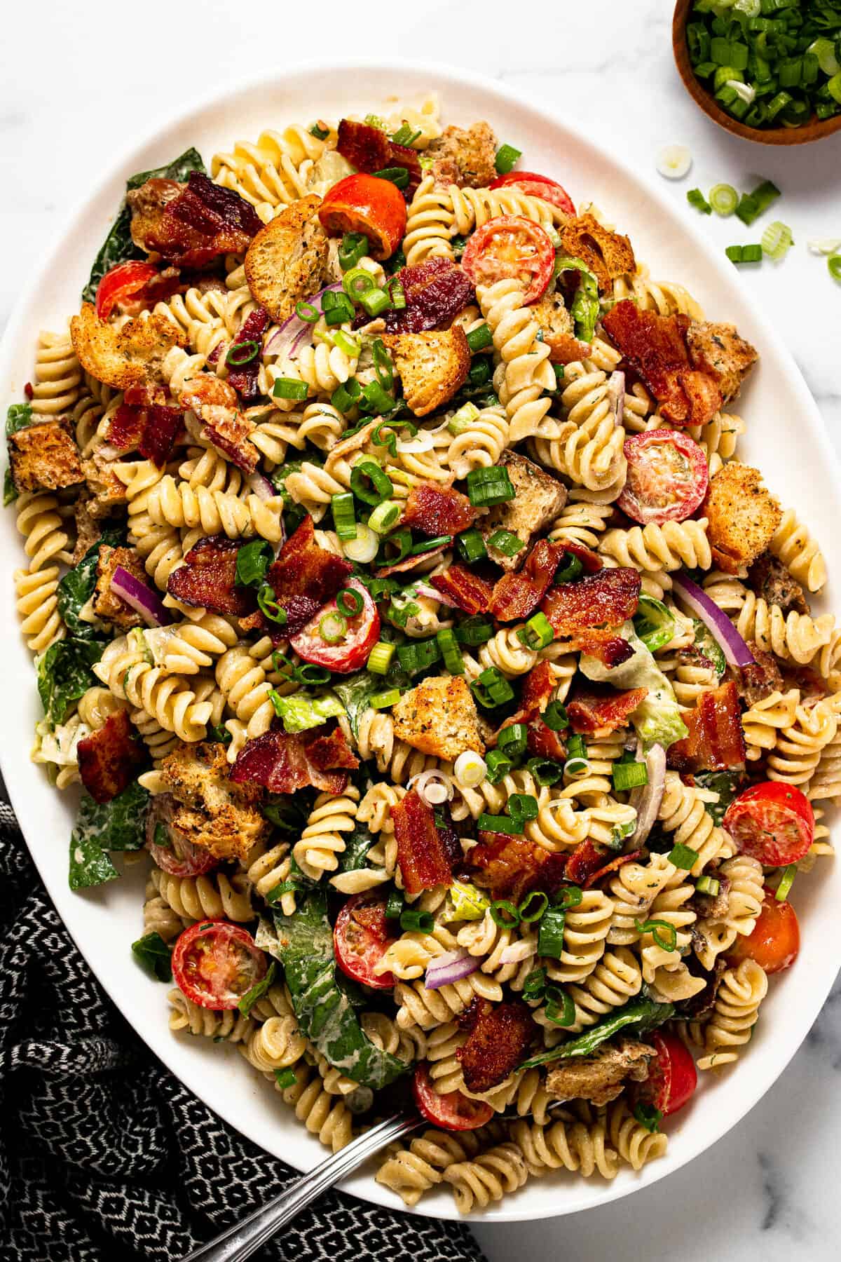 Large white platter filled with BLT pasta salad garnished with green onion
