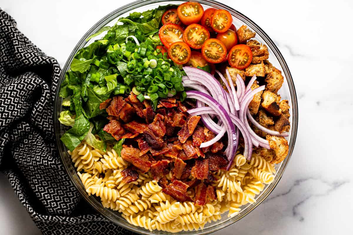 Large glass bowl filled with ingredients to make BLT pasta salad