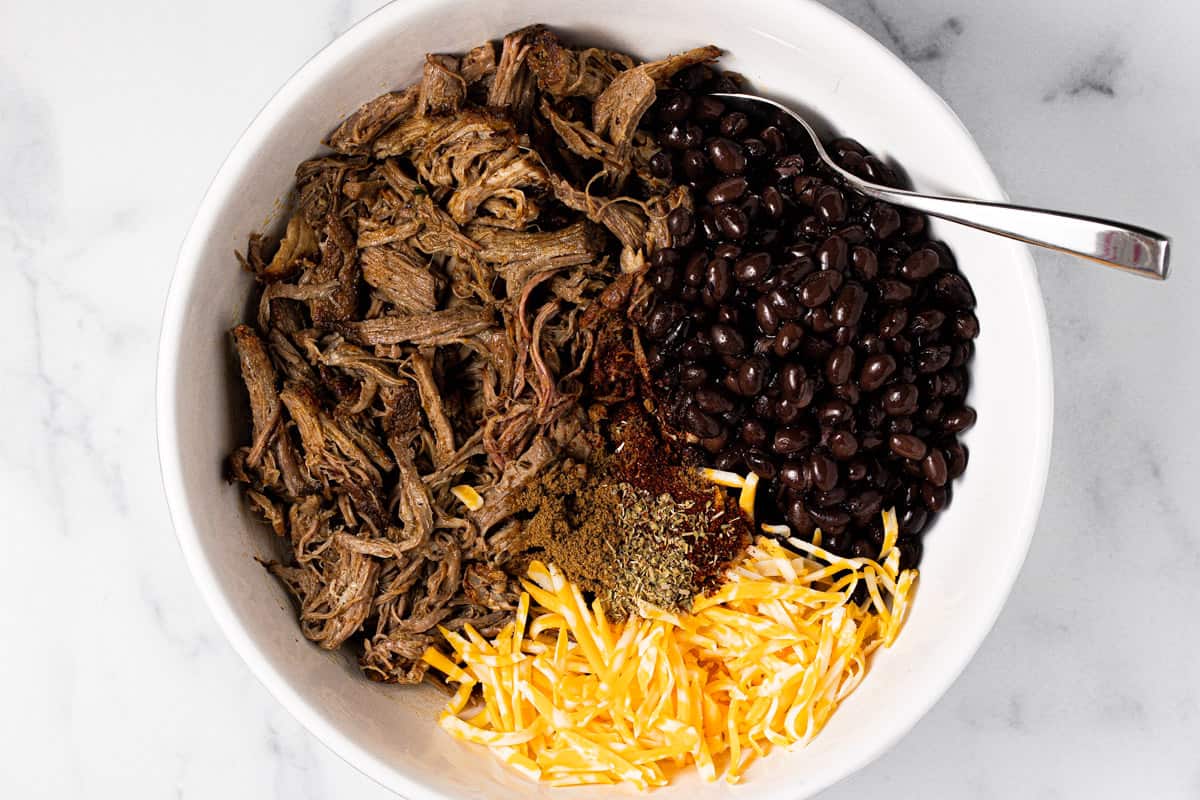 Large white bowl with pulled pork black beans and cheese to fill enchiladas
