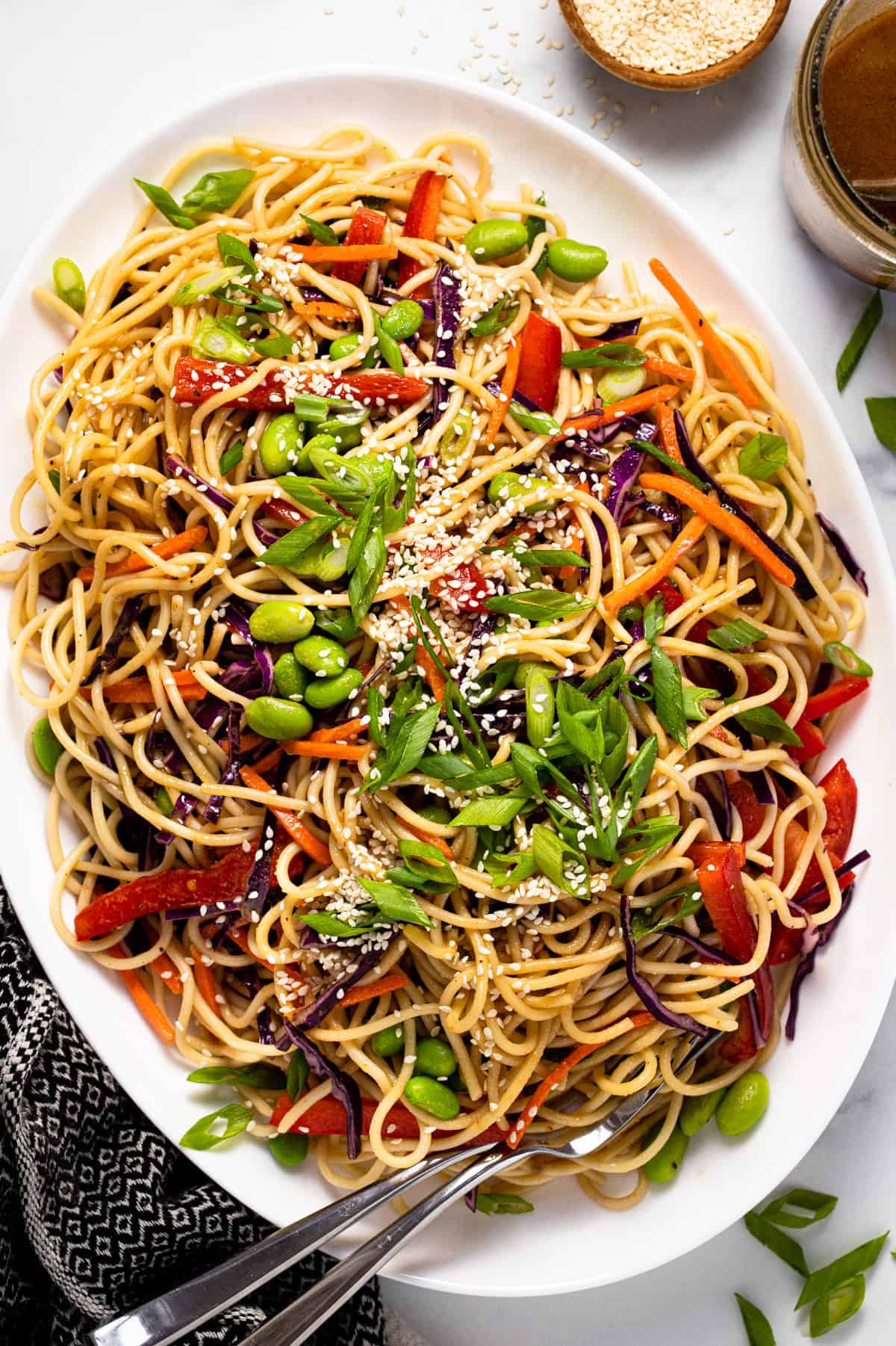 Large white serving platter filled with sesame noodle salad garnished with green onions