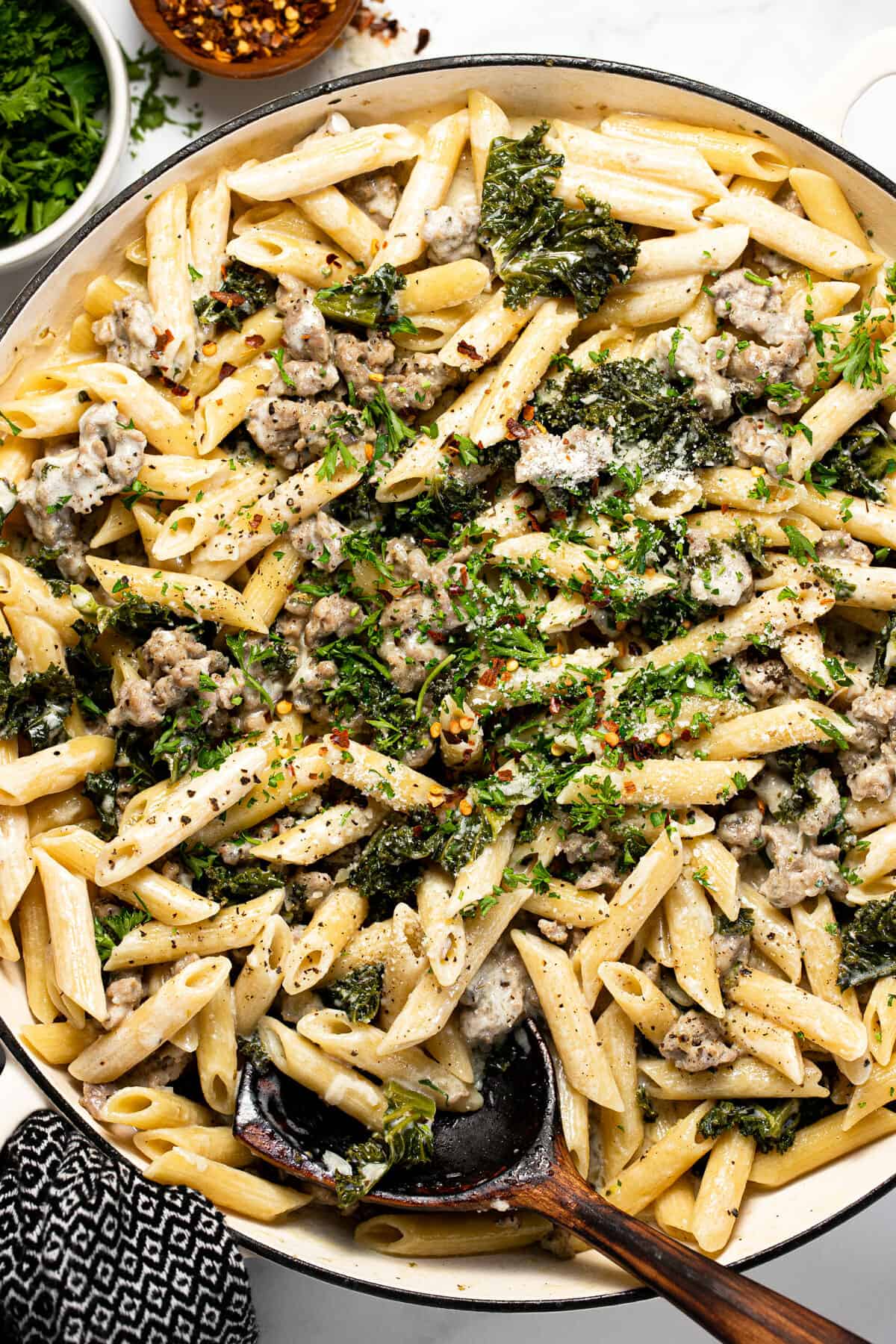 Large white pan filled with Italian sausage and kale pasta garnished with parsley