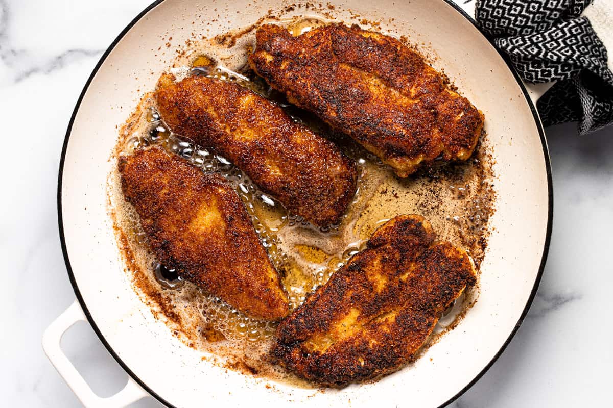 Breaded chicken breast frying in oil in a large white pan