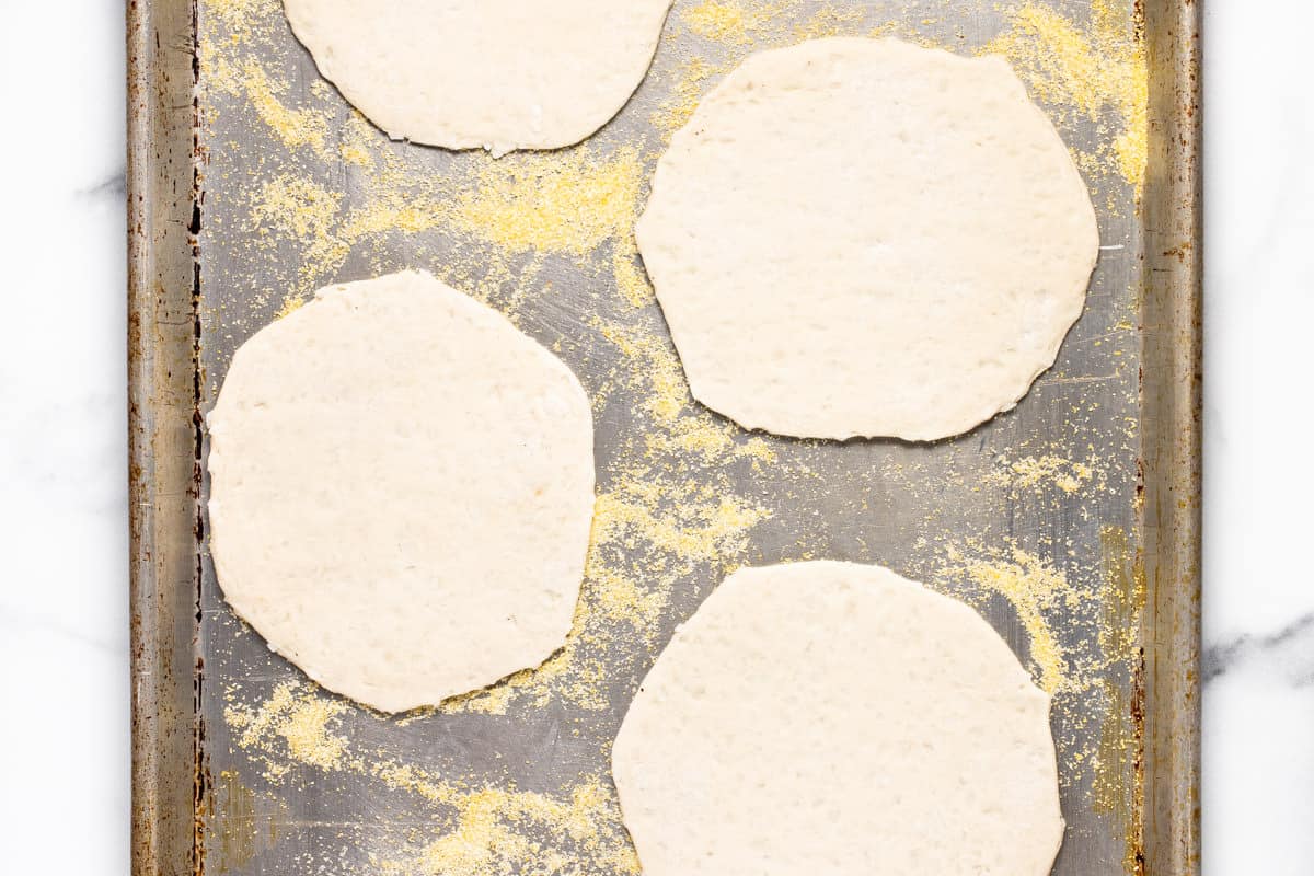 Biscuit dough pizza crusts on a cornmeal dusted baking sheet