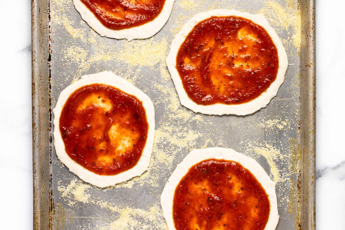 Mini pizzas with tomato sauce on a baking sheet