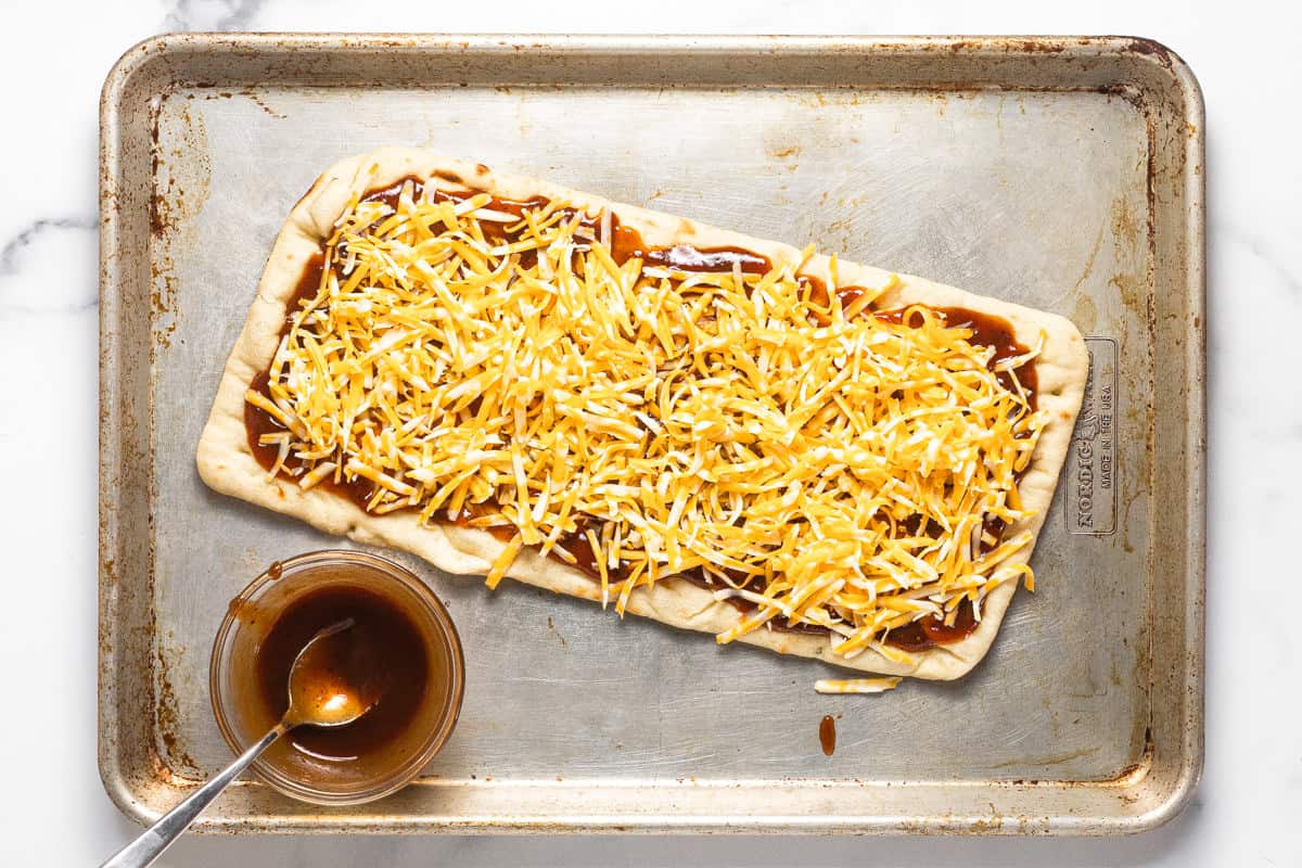 Baking sheet with a flatbread crust spread with BBQ sauce and cheese