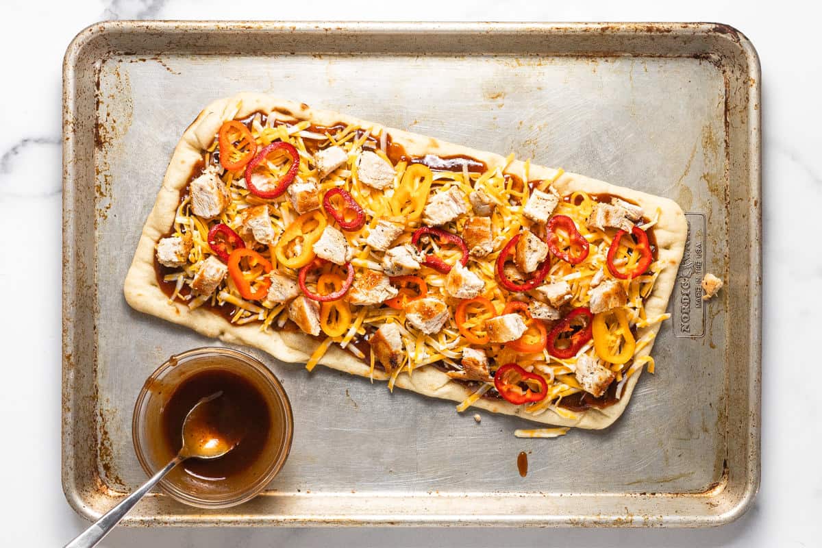 Unbaked BBQ chicken flatbread on a large baking sheet