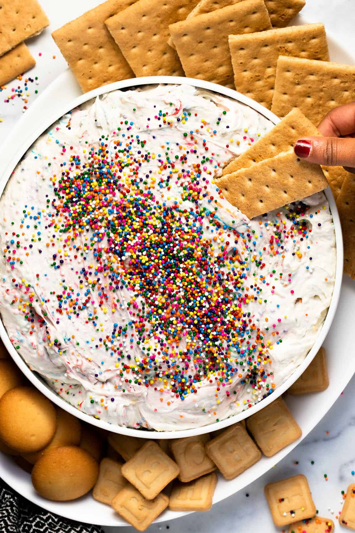 White serving bowl with creamy Dunkaroo dip with graham crackers dipped in it