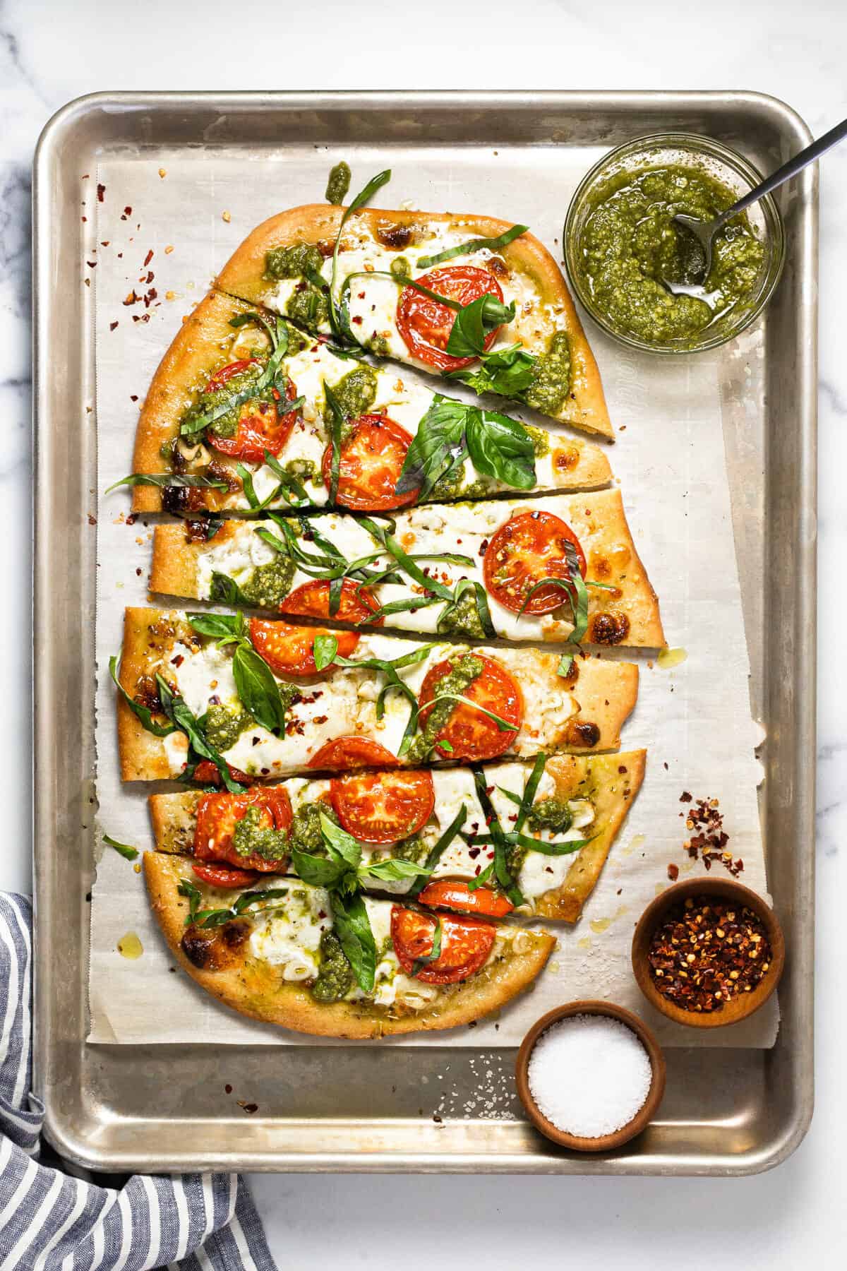 A baking sheet with sliced margherita flatbread pizza garnished with basil