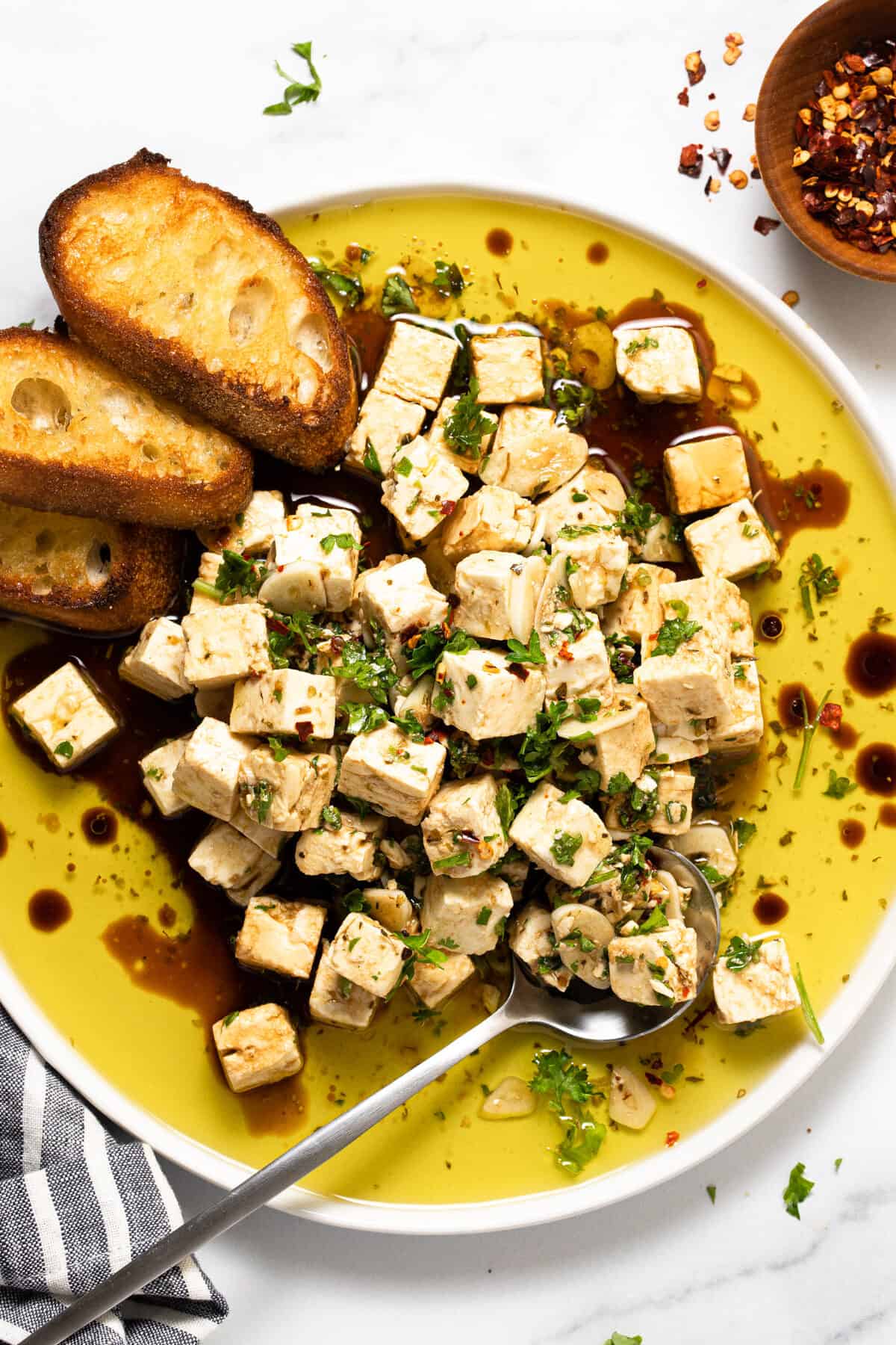 White plate filled with marinated squares of feta garnished with parsley