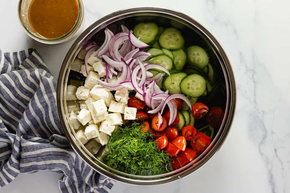 Large metal bowl filled with ingredients to make Greek cucumber salad