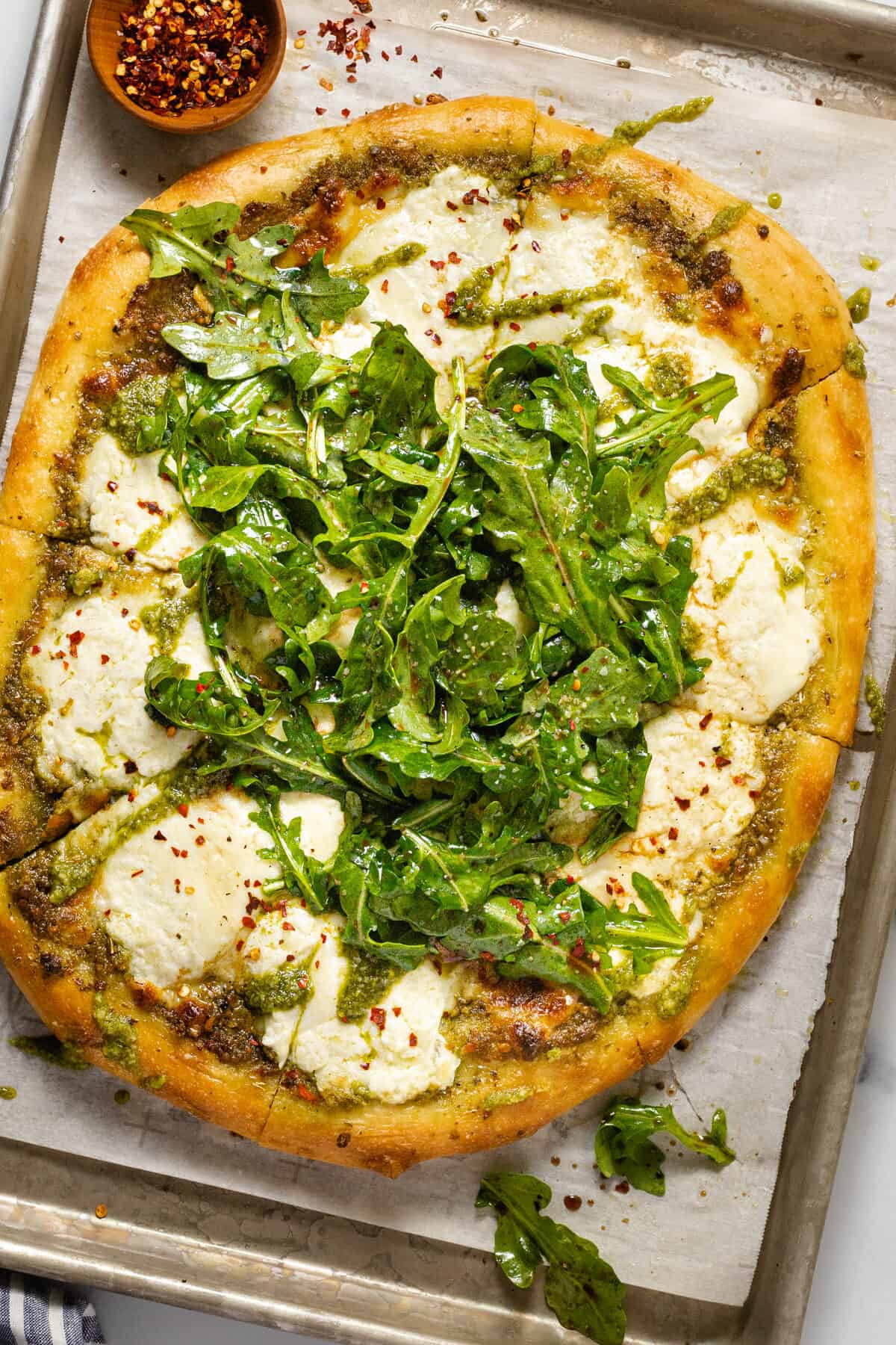 Parchment lined baking sheet with homemade burrata pizza garnished with arugula