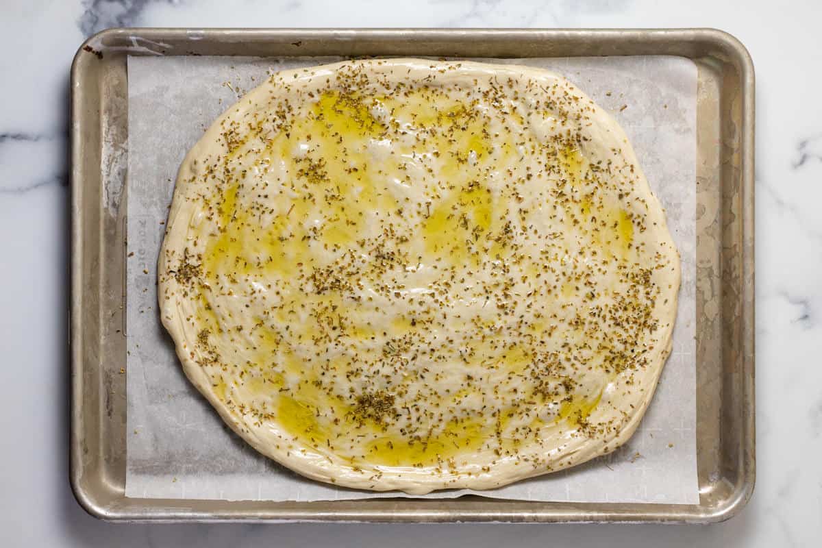 Parchment lined sheet pan with pizza dough topped with olive oil and oregano