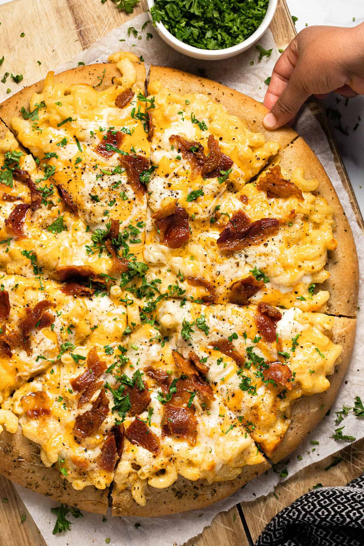 A hand reaching for a slice of mac and cheese pizza with bacon